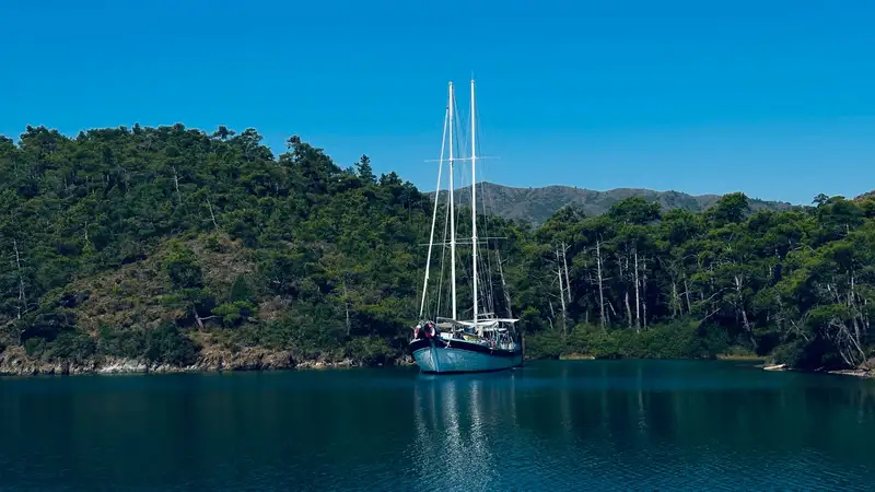 A beautiful yacht anchored in a tranquil cove surrounded by lush green hills, showcasing the natural beauty of Turkey.