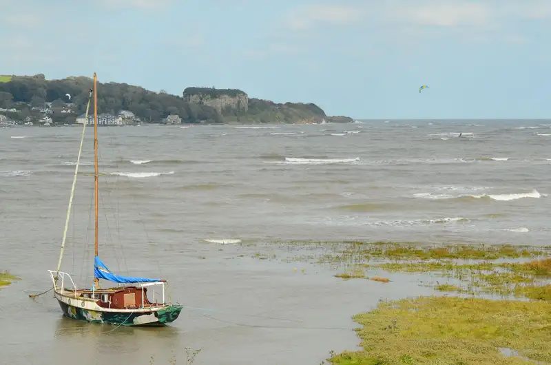 Scenic view of a single sailboat moored on a grassy coastal area with gentle waves.