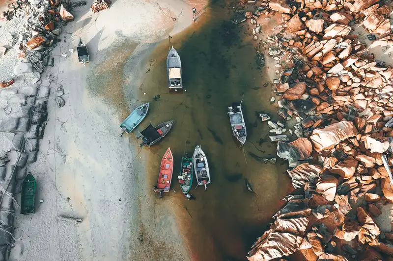 Drone view of fishing boats moored on sea water between sandy and rocky shores in daylight