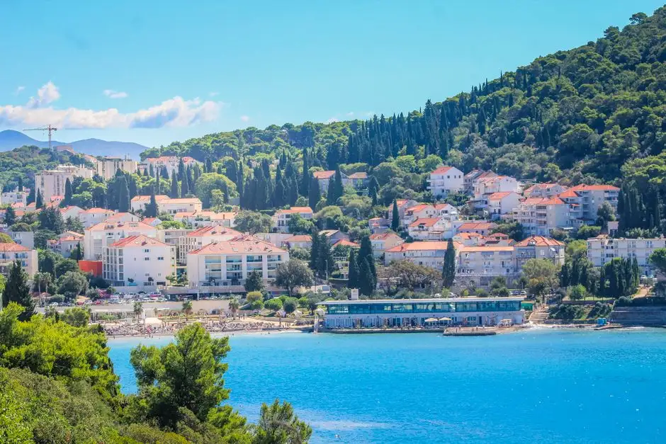 Charming Mediterranean coastal village with white buildings, lush greenery, and a bright blue sea.