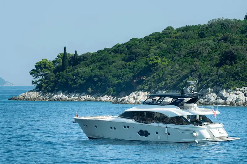 Elegant yacht sailing on the Adriatic Sea near Dubrovnik, Croatia, with lush greenery in the background.