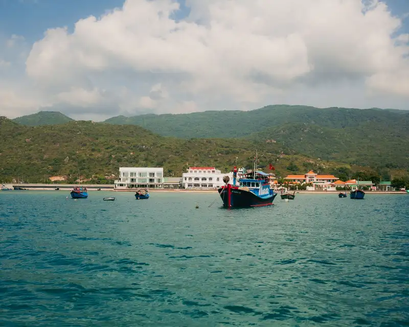 View of boats in a serene harbor at Phan Rang–Tháp Chàm, Vietnam, against lush hills.